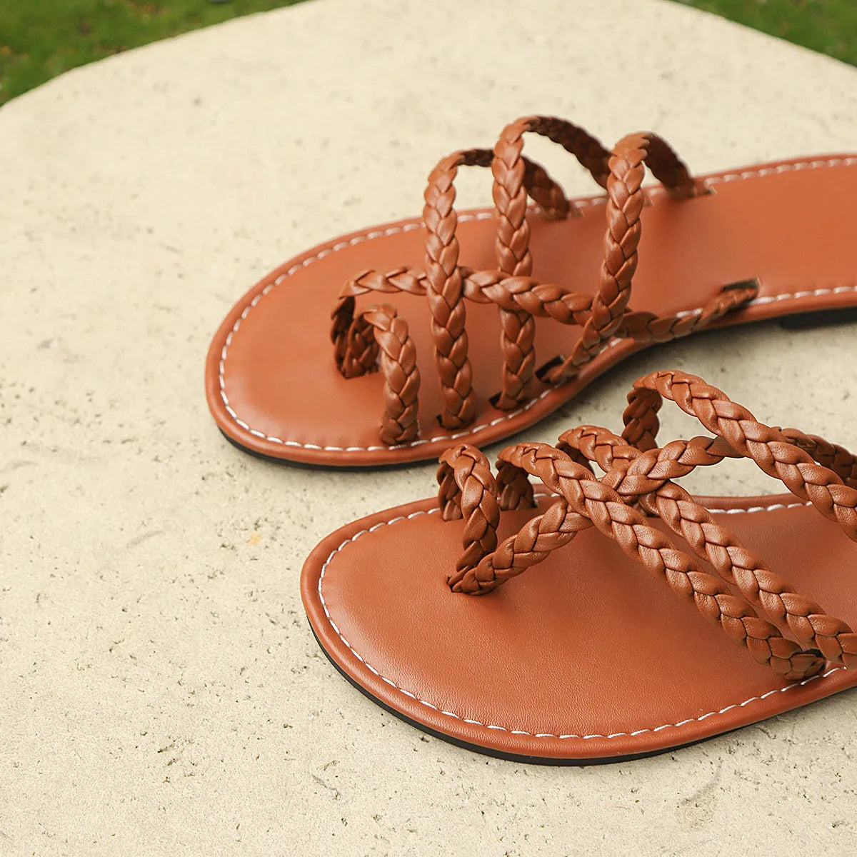 Women's brown woven Roman sandals with a clip-toe and flat rubber sole on a white background.