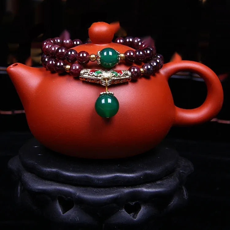 Close-up of a natural deep red garnet bead bracelet with a golden toad charm and double ring clasp.