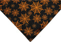 Black and orange reversible Halloween dog bandana with pumpkin and spider web patterns, showing adjustable fastening.