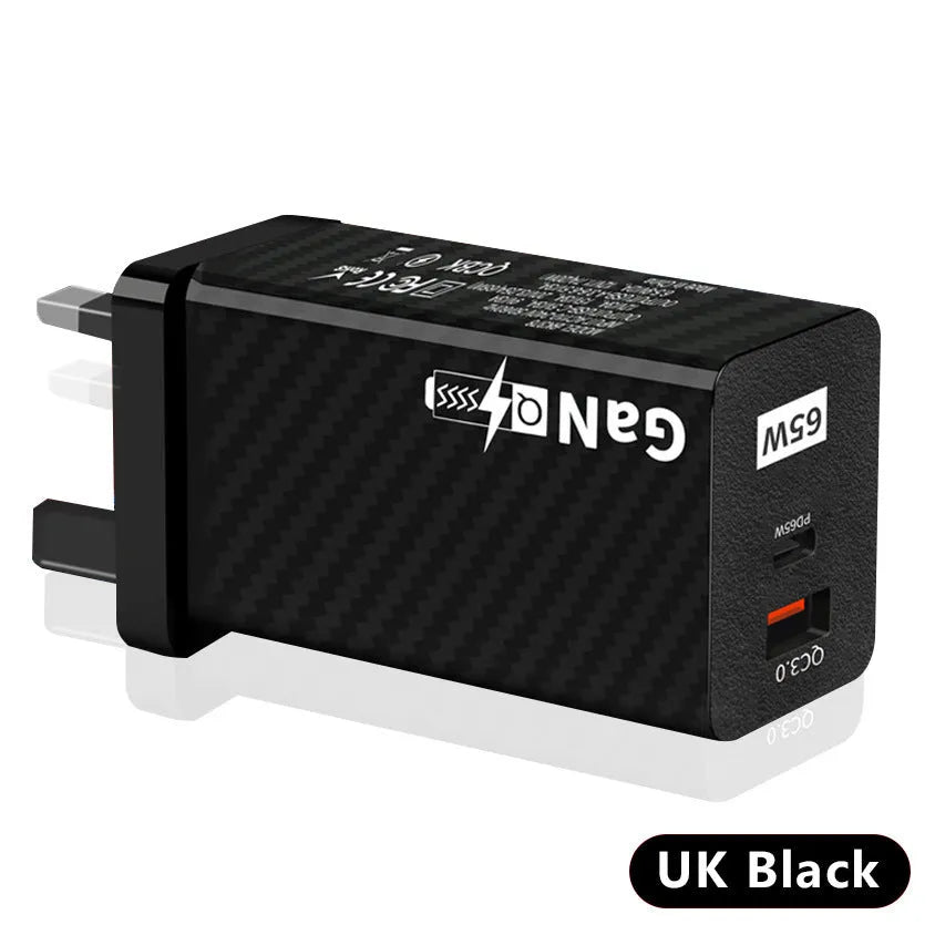 Compact white 65W Gallium Nitride laptop charger with UK, US and EU plug attachments on a desk.