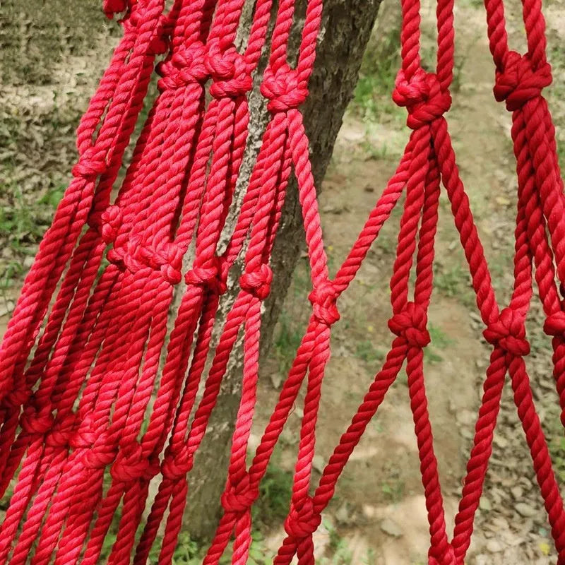 Green nylon rope mesh hammock hung between two trees showing its woven texture and length.