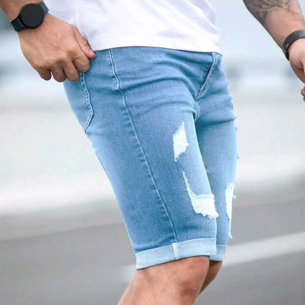 Men's sky blue denim shorts with distressed multi-hole design, low waist, and zip fly opening