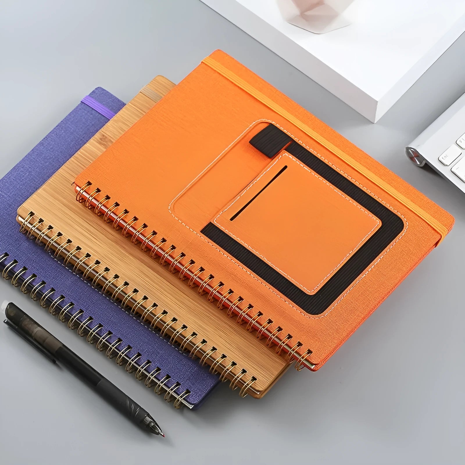 Erasable coil notebook with stone paper, showing a black cover option and a pen on a wooden desk.