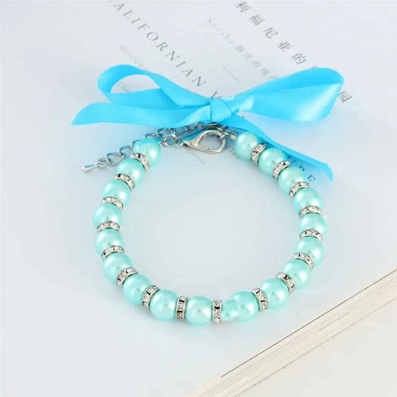 Small dog wearing a blue adjustable pearl and rhinestone necklace with a ribbon bow