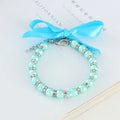 Small dog wearing a blue adjustable pearl and rhinestone necklace with a ribbon bow
