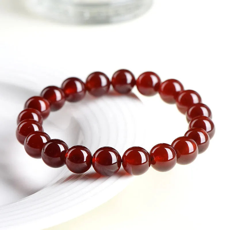 Natural orange red garnet ball bead bracelet with ruyi charms on a wrist.