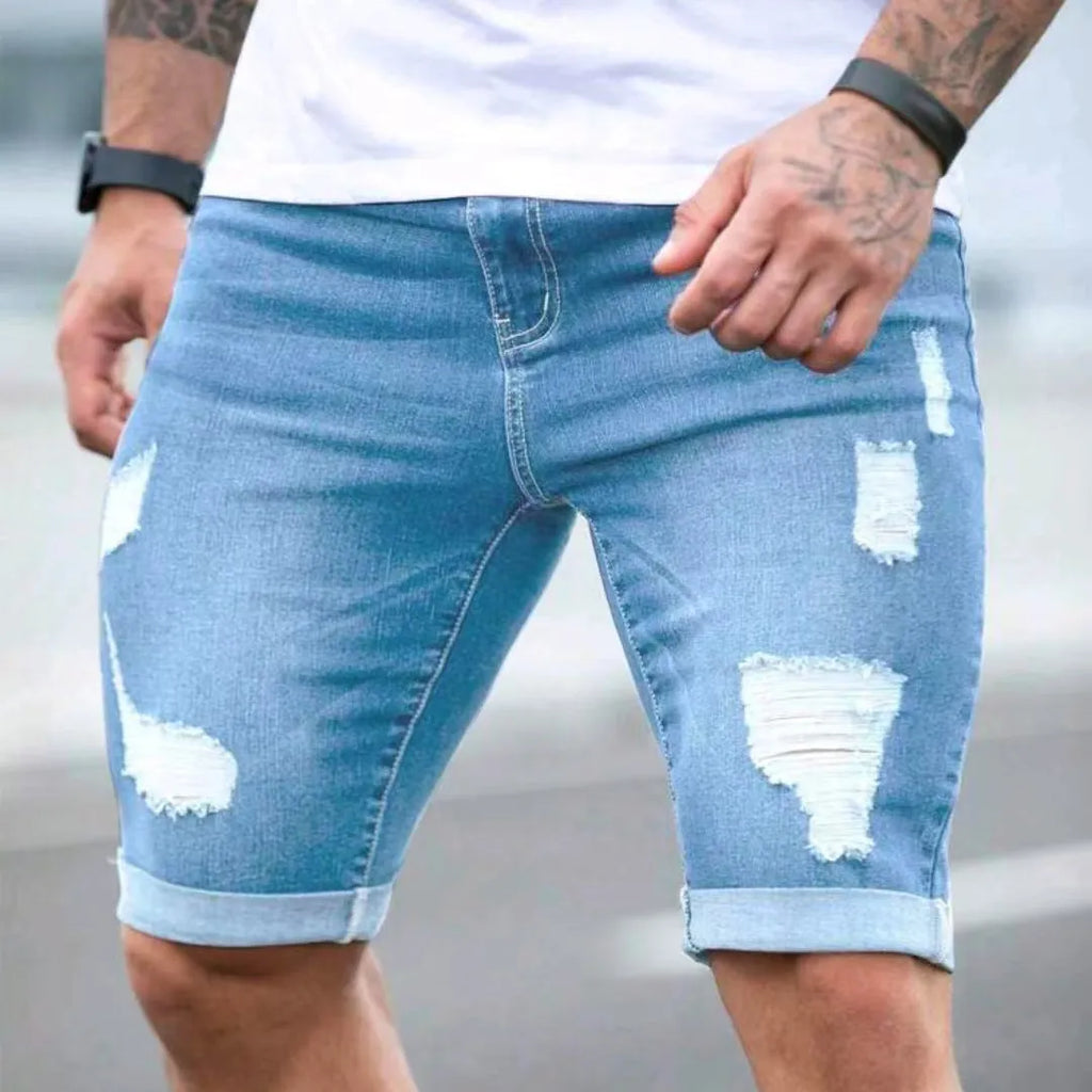 Men's sky blue denim shorts with distressed multi-hole design, low waist, and zip fly opening