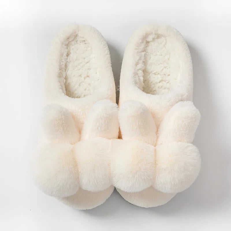 Women's fluffy bunny slippers with rabbit fur upper in cream colour on a wooden floor.