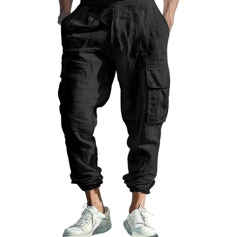 Man wearing loose-fit linen trousers with ankle-tied cuffs and a multi-pocket tether detail.