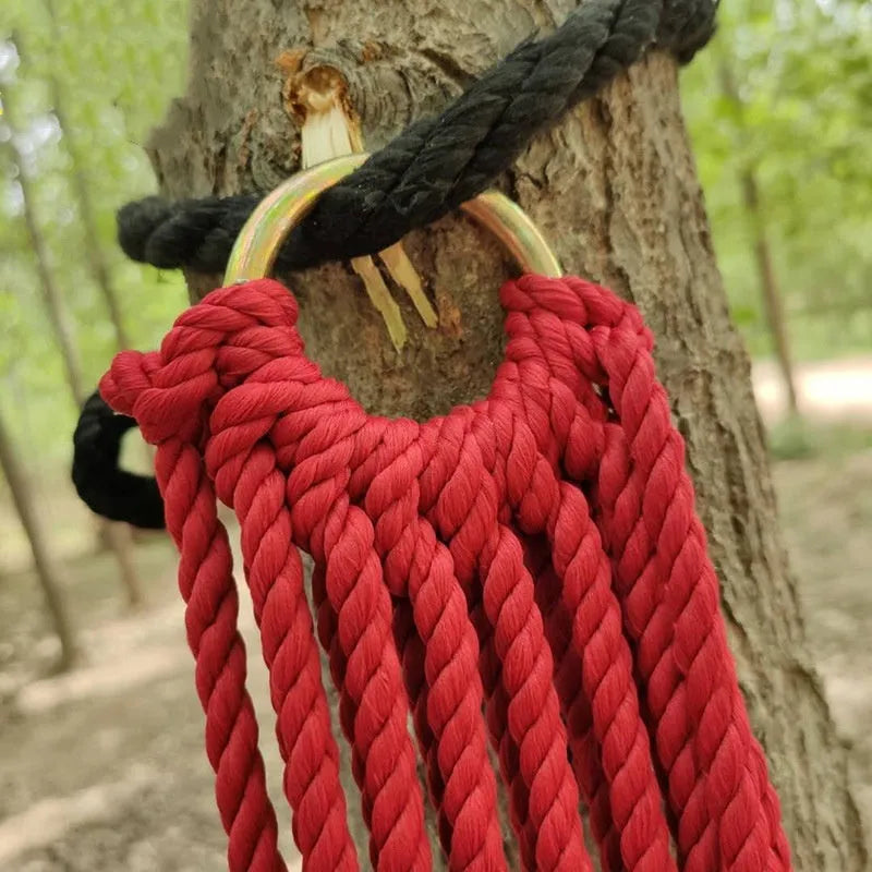 Green nylon rope mesh hammock hung between two trees showing its woven texture and length.