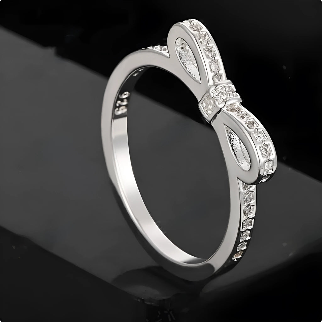 Silver colour bow-shaped ring with rhinestone and zircon crystal decoration on a finger.
