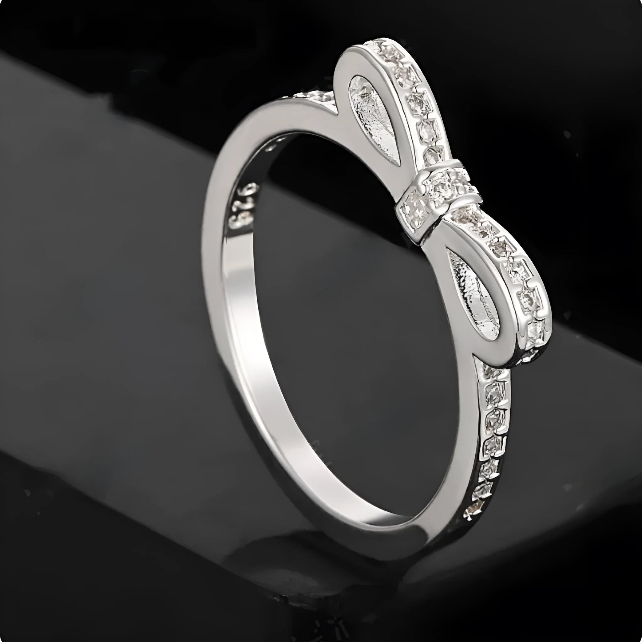 Silver colour bow-shaped ring with rhinestone and zircon crystal decoration on a finger.