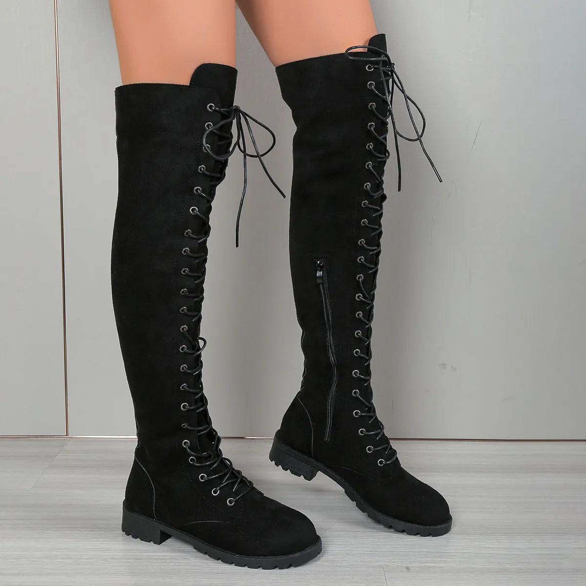 Black lace-up over-the-knee boots with round toe and flat heel on a neutral background.