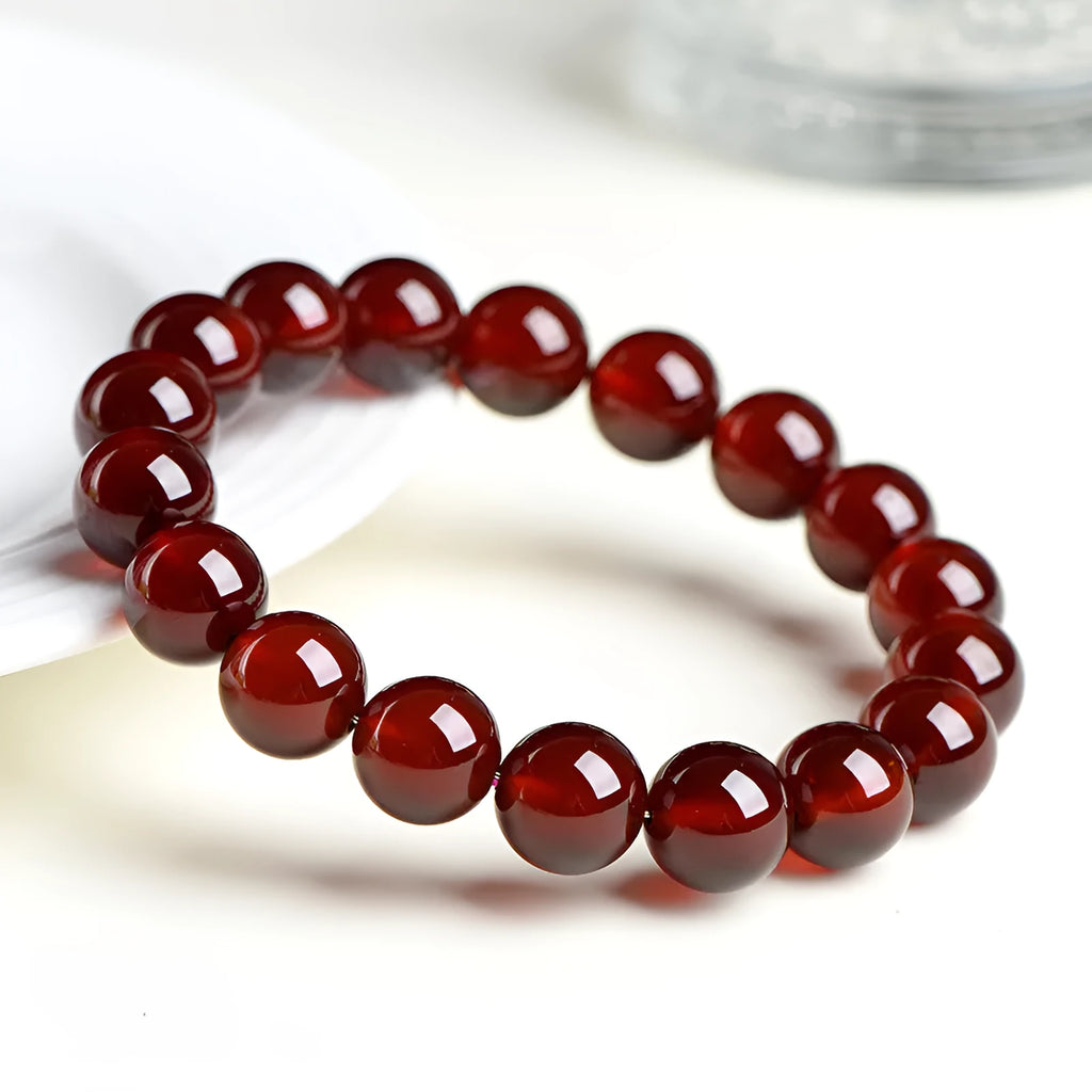 Natural orange red garnet ball bead bracelet with ruyi charms on a wrist.