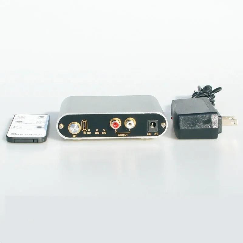 Silver aluminium audio source selector switch with infrared remote control on a shelf.
