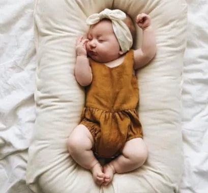 Beige portable cotton baby nest crib for newborn infants on a bed.