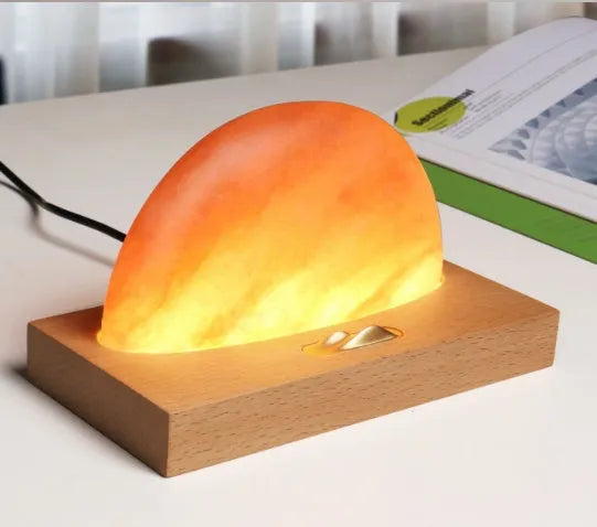 Natural crystal salt lamp with wireless charging pad on a light beech wood table base.