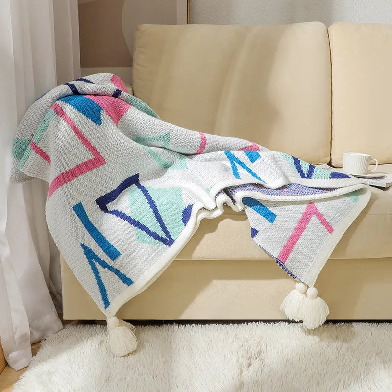 Bohemian style acrylic blanket with tassel fringe on a sofa, shown in a geometric print colour.