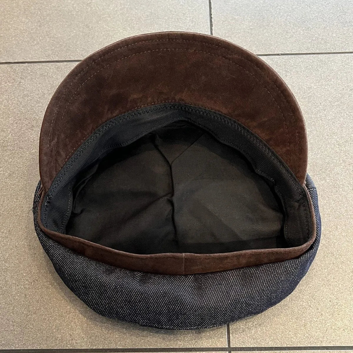 Dark blue denim newsboy cap with an adjustable strap, shown on a model