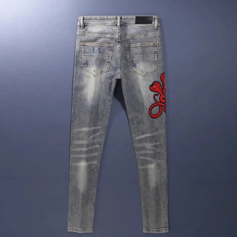 Men's slim fit jeans in old colour with distressed holes and embroidered patches on the legs.