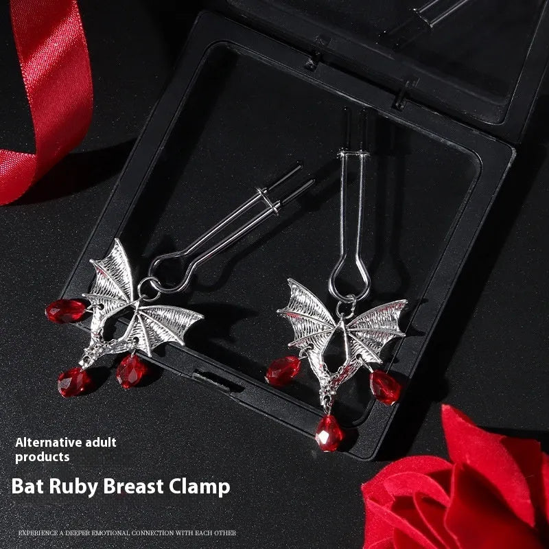 A pair of silver metal bat-shaped adjustable nipple clamps on a plain background.