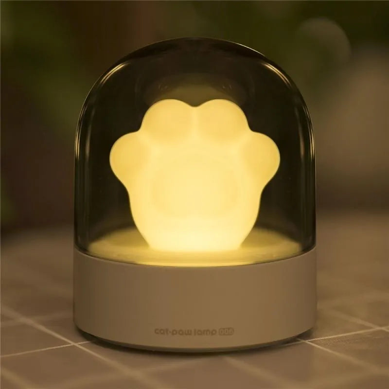 Grey and pink cat paw shaped USB rechargeable night light with adjustable brightness on a desk.
