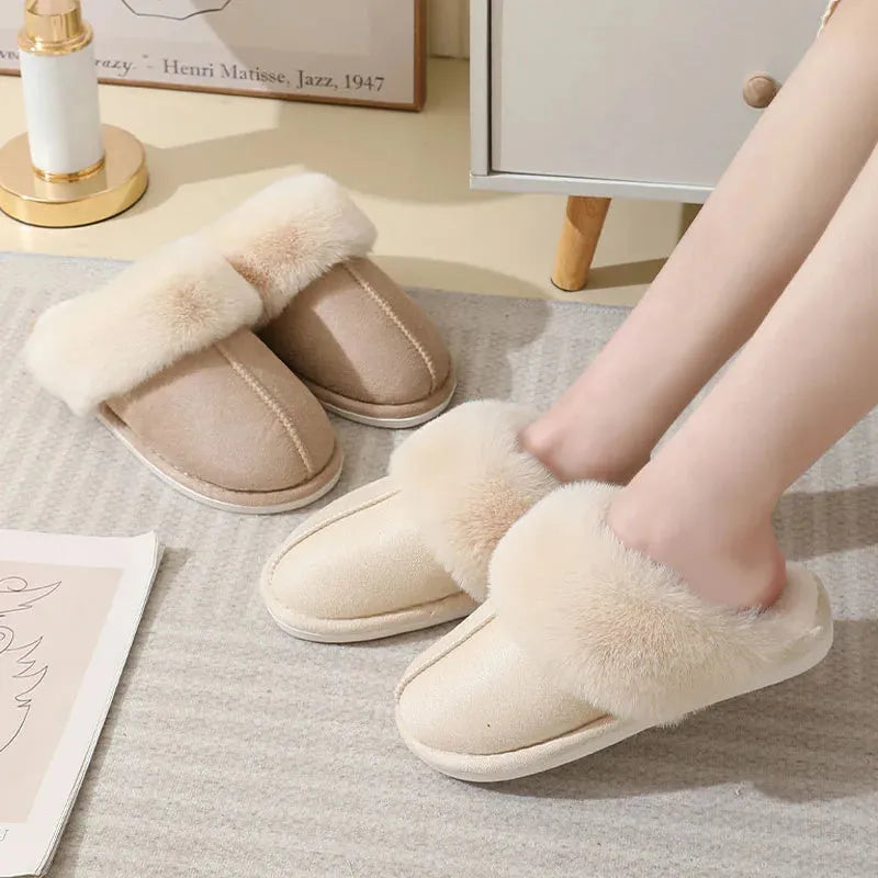 Women's brown plush winter slippers with round toe and flat heel on a wooden floor.