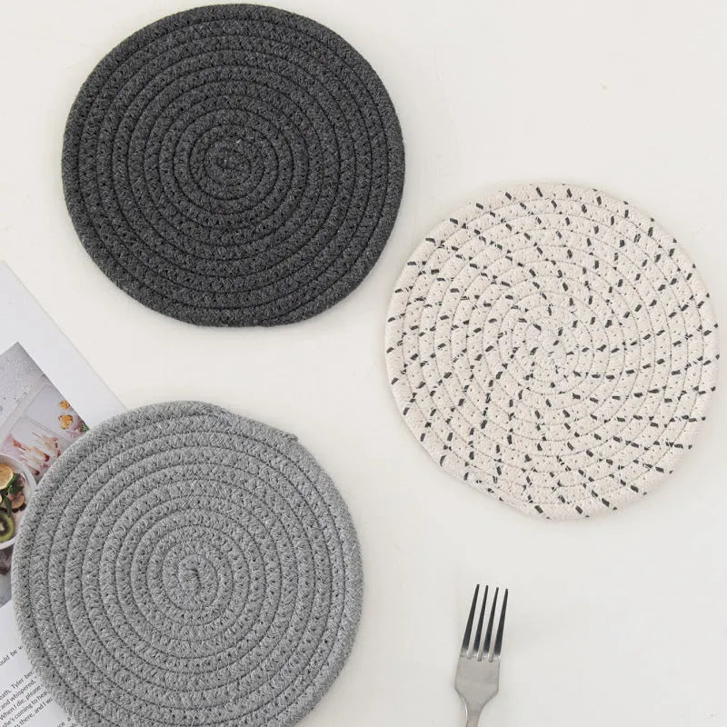 Set of three round grey cotton cord coaster placemats on a wooden table