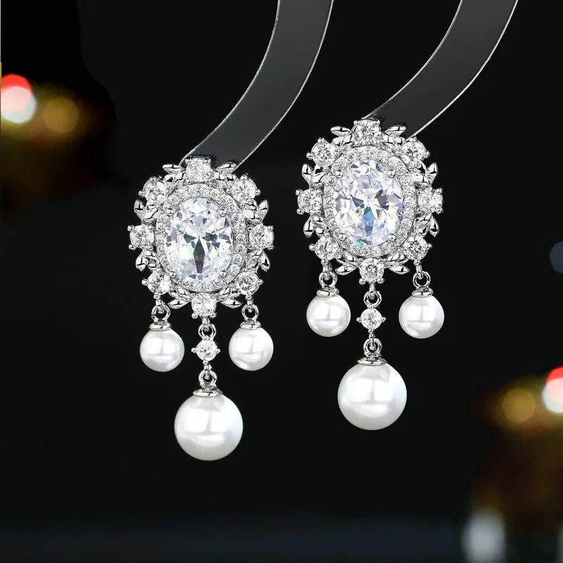 A pair of geometric ellipse-shaped drop earrings with a tassel, featuring pearls and inlaid zircon stones on copper.