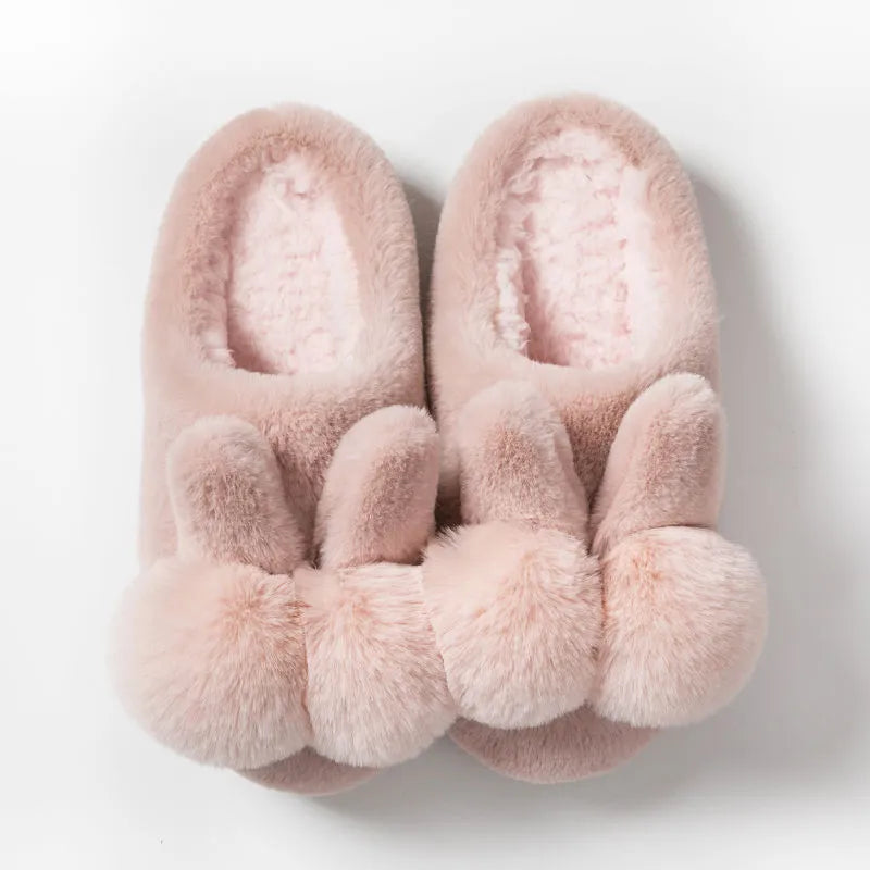 Women's fluffy bunny slippers with rabbit fur upper in cream colour on a wooden floor.