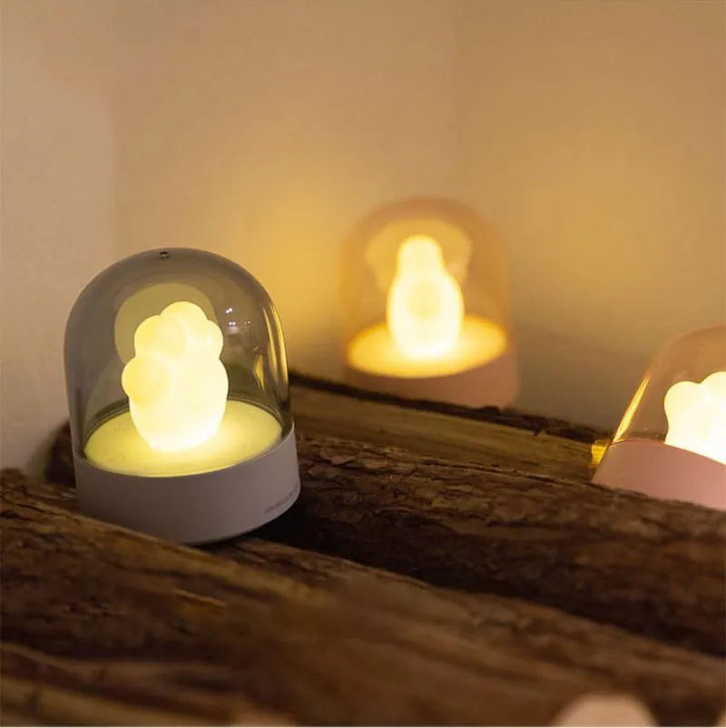 Grey and pink cat paw shaped USB rechargeable night light with adjustable brightness on a desk.