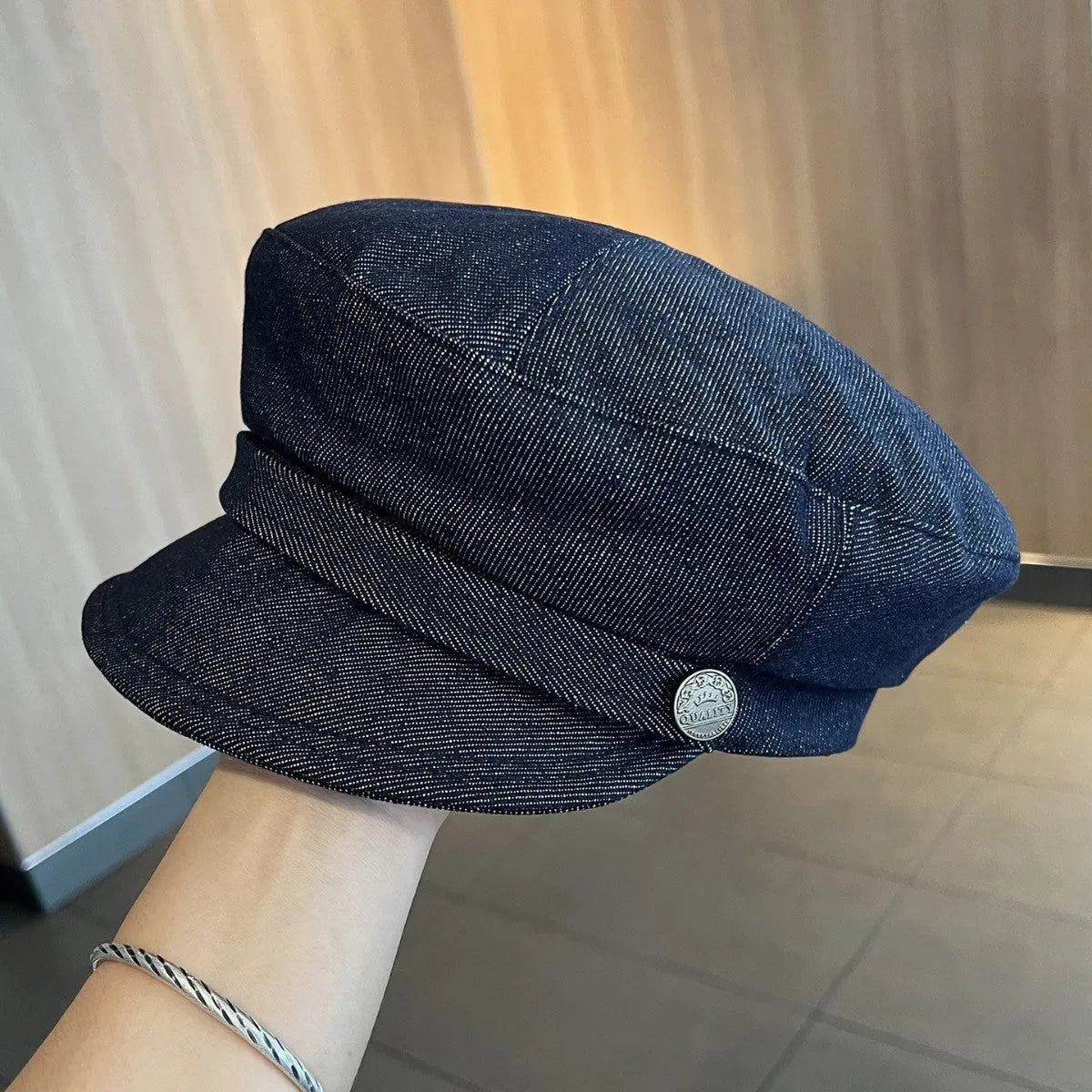Dark blue denim newsboy cap with an adjustable strap, shown on a model