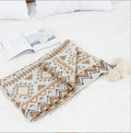 Bohemian style acrylic blanket with tassel fringe on a sofa, shown in a geometric print colour.