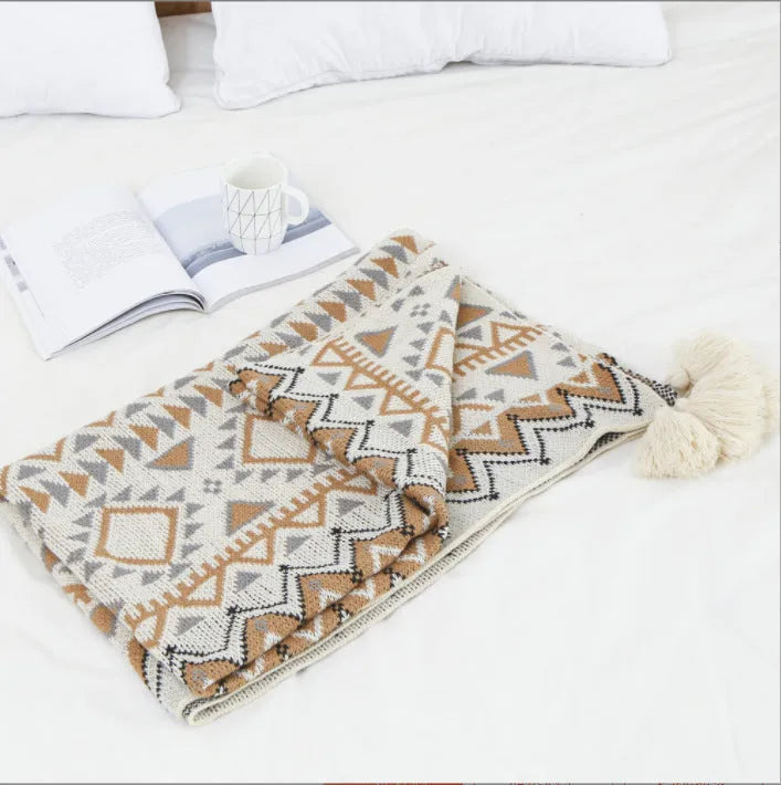 Bohemian style acrylic blanket with tassel fringe on a sofa, shown in a geometric print colour.