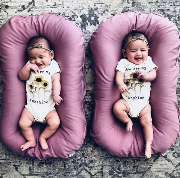 Beige portable cotton baby nest crib for newborn infants on a bed.