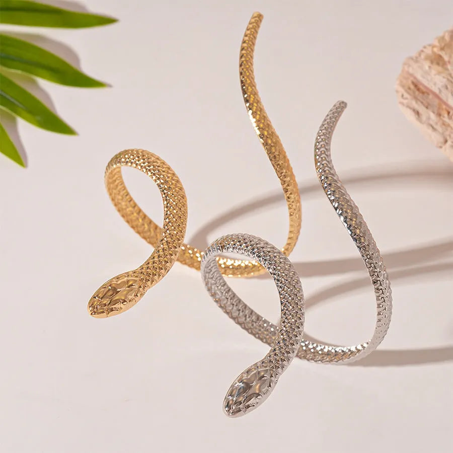 Gold twisted snake design metal bracelet and ring set on a white background.