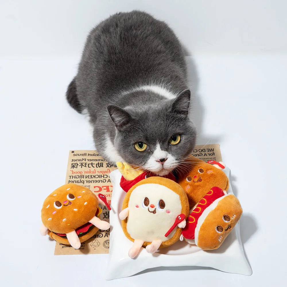 Set of four soft fabric cat chew toys shaped like a hamburger, chicken leg, fries, and hot dog on a plain background.