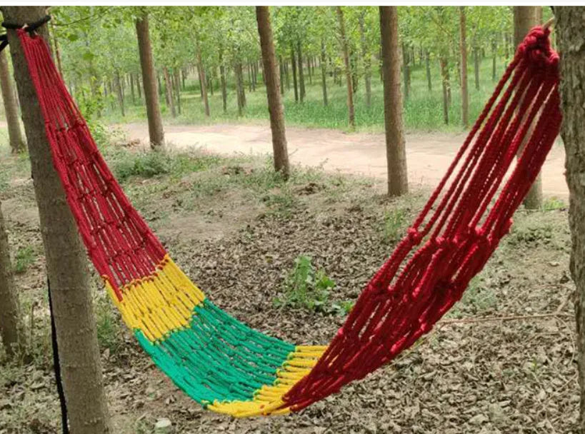Green nylon rope mesh hammock hung between two trees showing its woven texture and length.