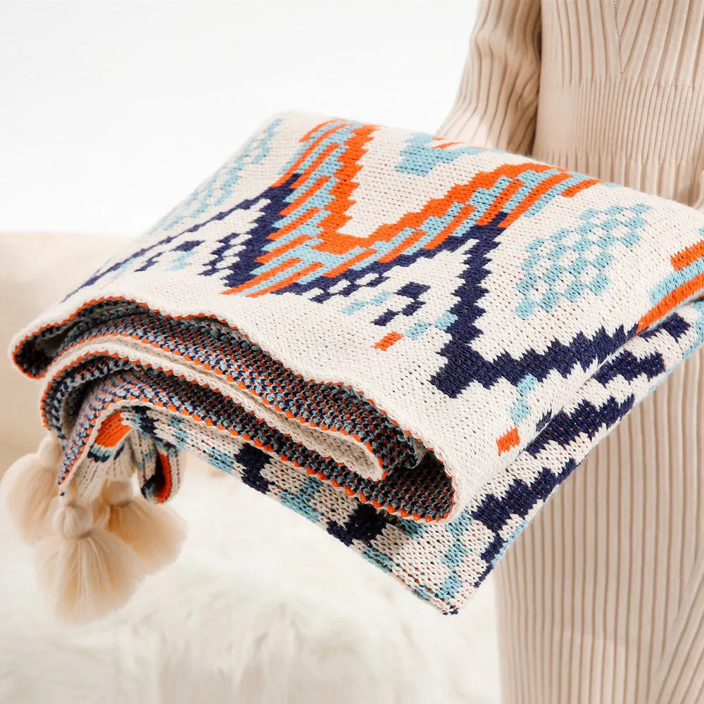 Bohemian style acrylic blanket with tassel fringe on a sofa, shown in a geometric print colour.