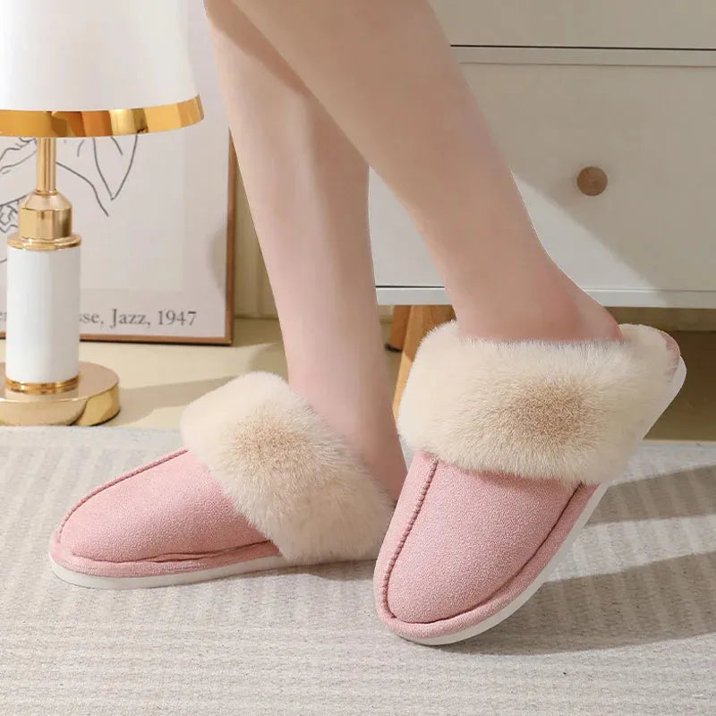 Women's brown plush winter slippers with round toe and flat heel on a wooden floor.