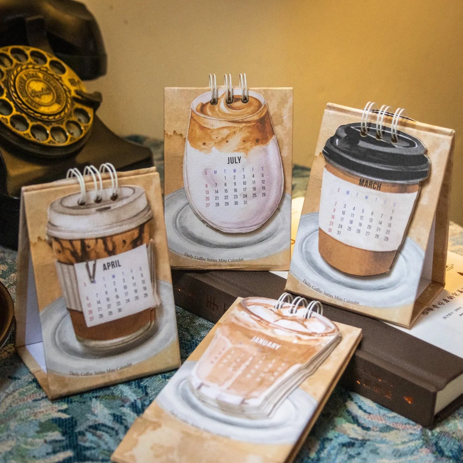 Coffee themed mini desk calendar for 2025 showing four different model designs on a desk.