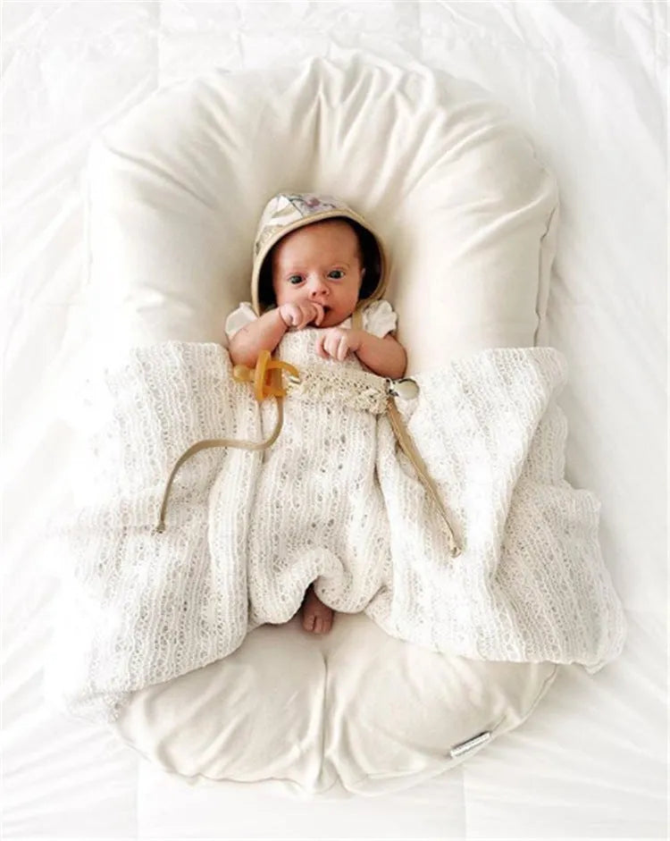 Beige portable cotton baby nest crib for newborn infants on a bed.