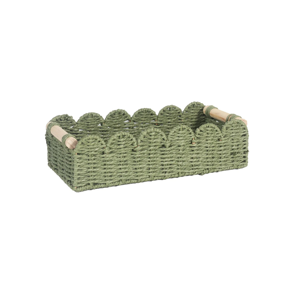 A woven paper storage basket in a neutral colour on a wooden desktop, holding remote controls and pens.