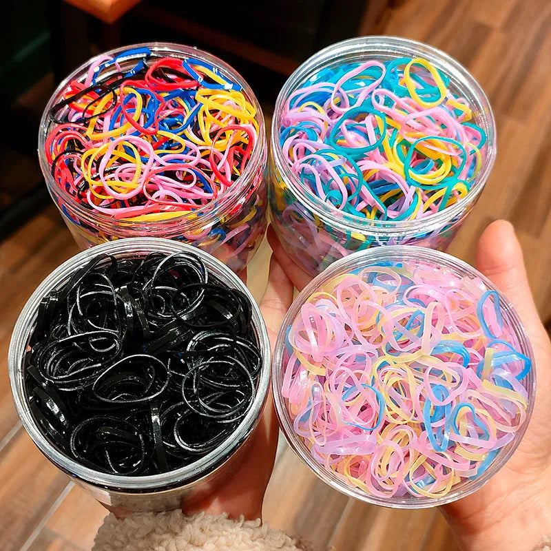 Assortment of colourful small TPU baby hair ties in a reusable plastic container.