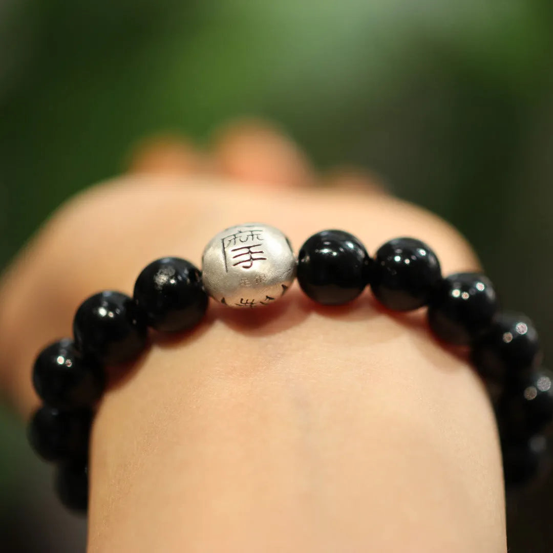 Close-up of a black agate and sterling silver bracelet with 10mm beads and a manual polish finish.