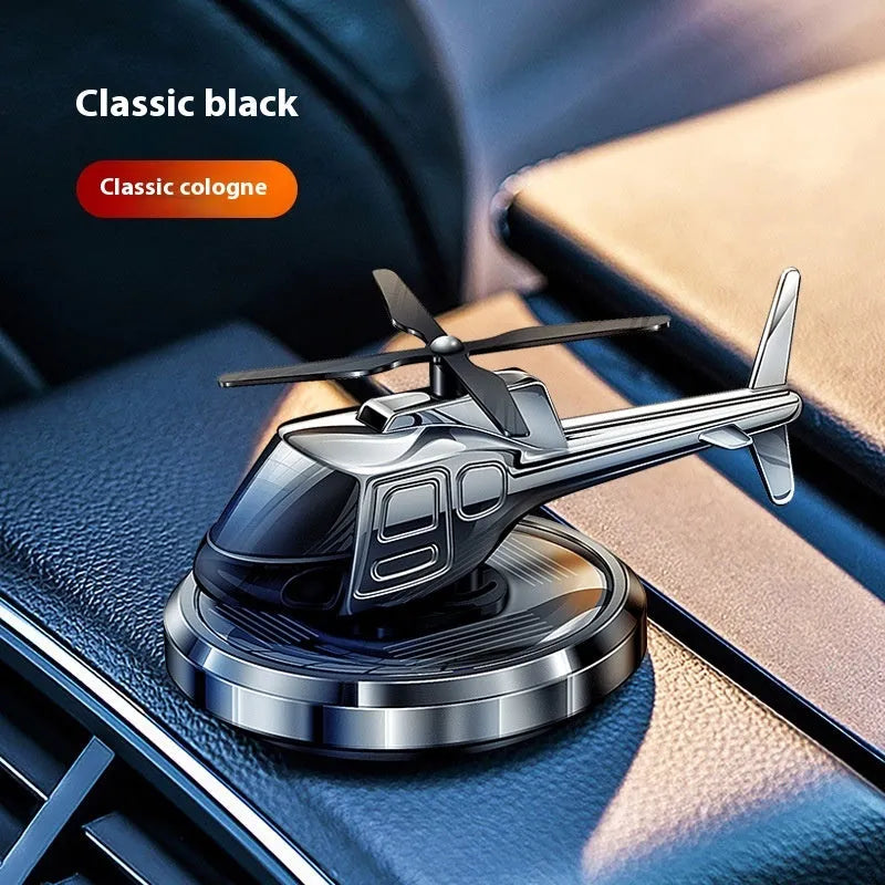 Silver solar-powered metal helicopter car air freshener ornament with rotating blades on a dashboard.