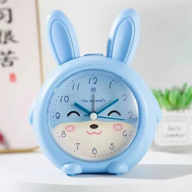 Pink and blue cartoon-style children's singing alarm clock with night light on a bedside table.