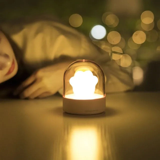 Grey and pink cat paw shaped USB rechargeable night light with adjustable brightness on a desk.