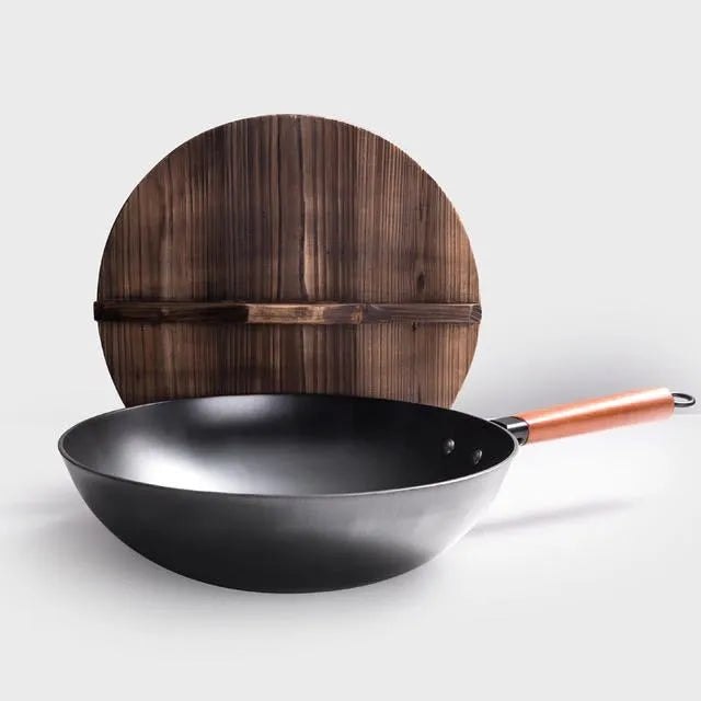 Traditional black iron wok pan with a wooden handle on a hob.