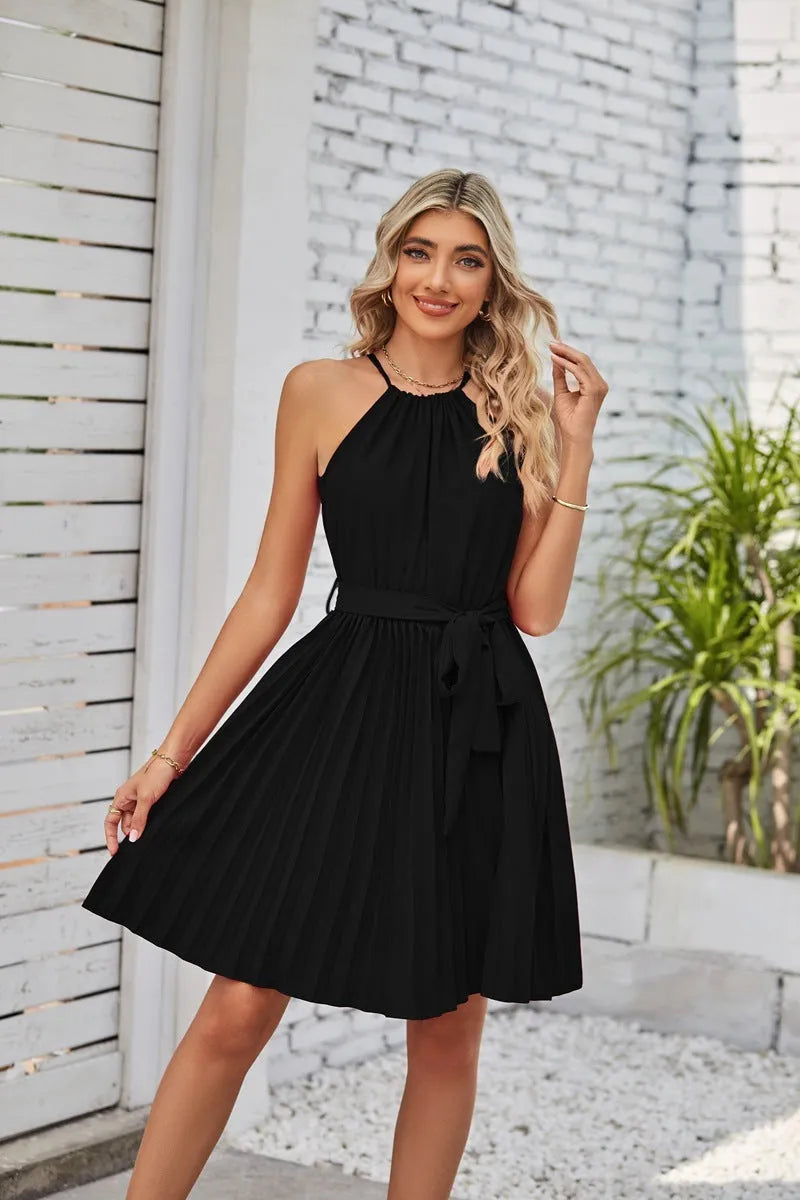 Woman wearing a black halter neck chiffon sundress with a pleated skirt and an adjustable waist tie.